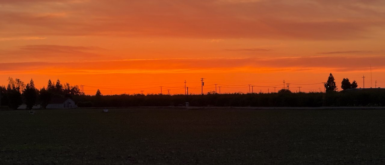Open Central Valley farmland under a wide sky as the sun drops toward the horizon.